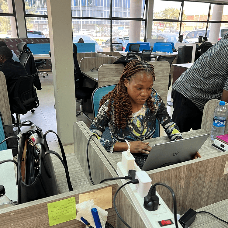 Young woman working on a laptop in a busy office environment.