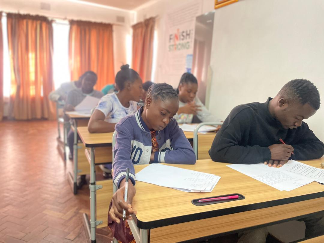 Students focused on writing at desks in a classroom.