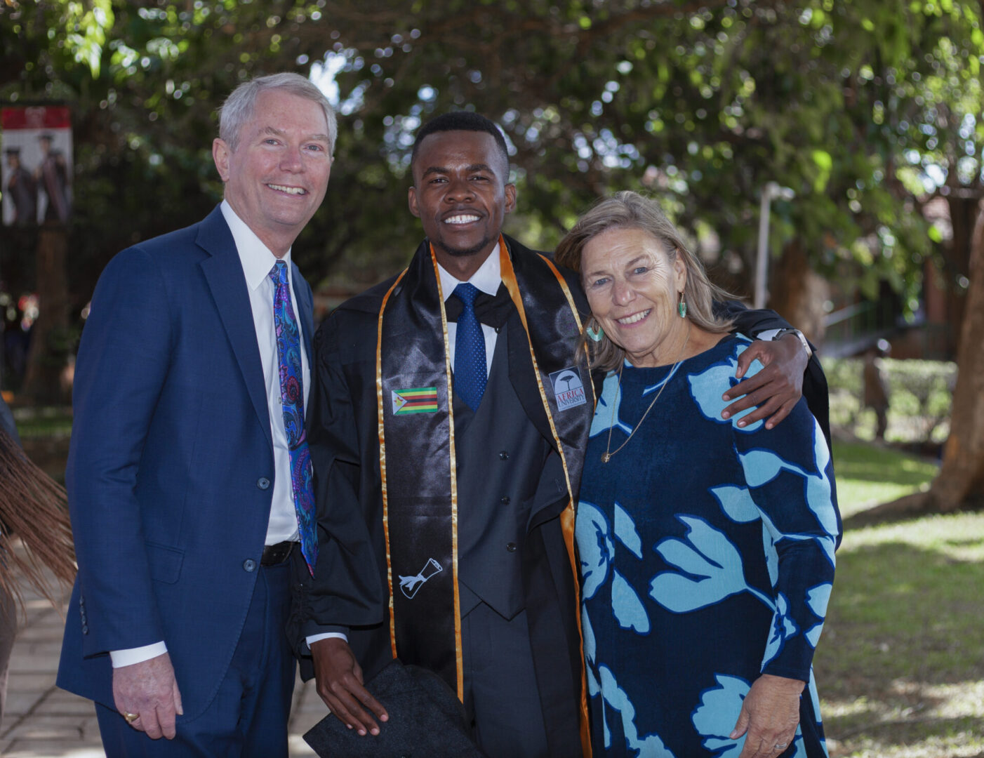 A graduate with two adults posing outdoors, smiling.