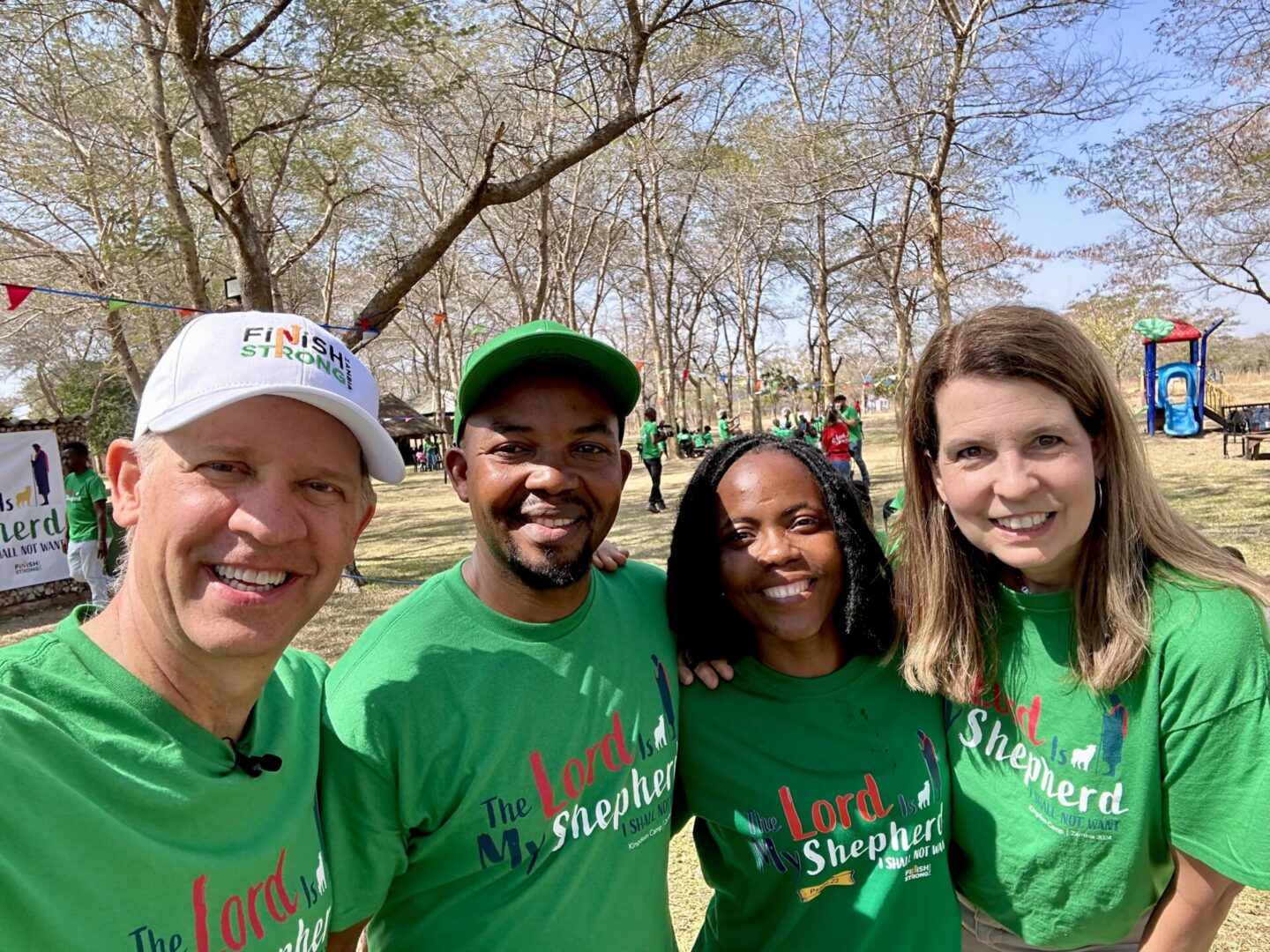 Four people smiling outdoors, wearing matching green shirts for a group event.
