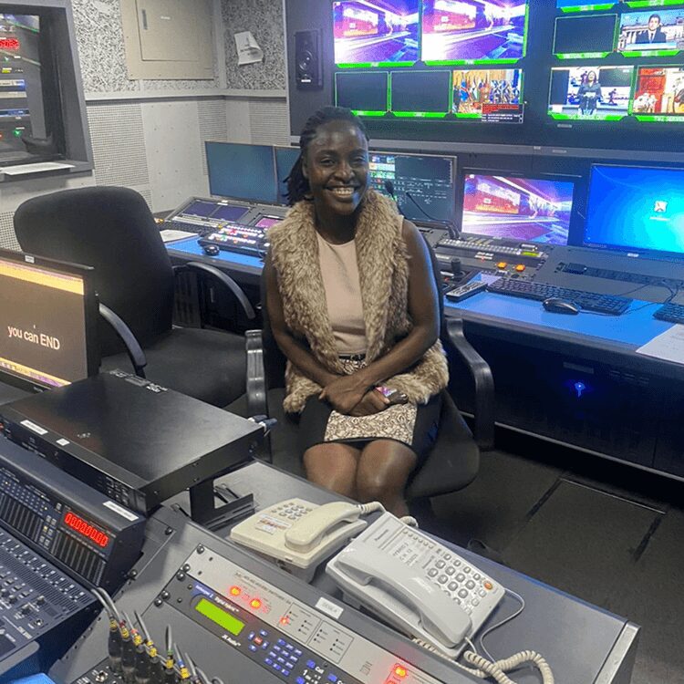 A woman smiling in a TV control room with multiple monitors.
